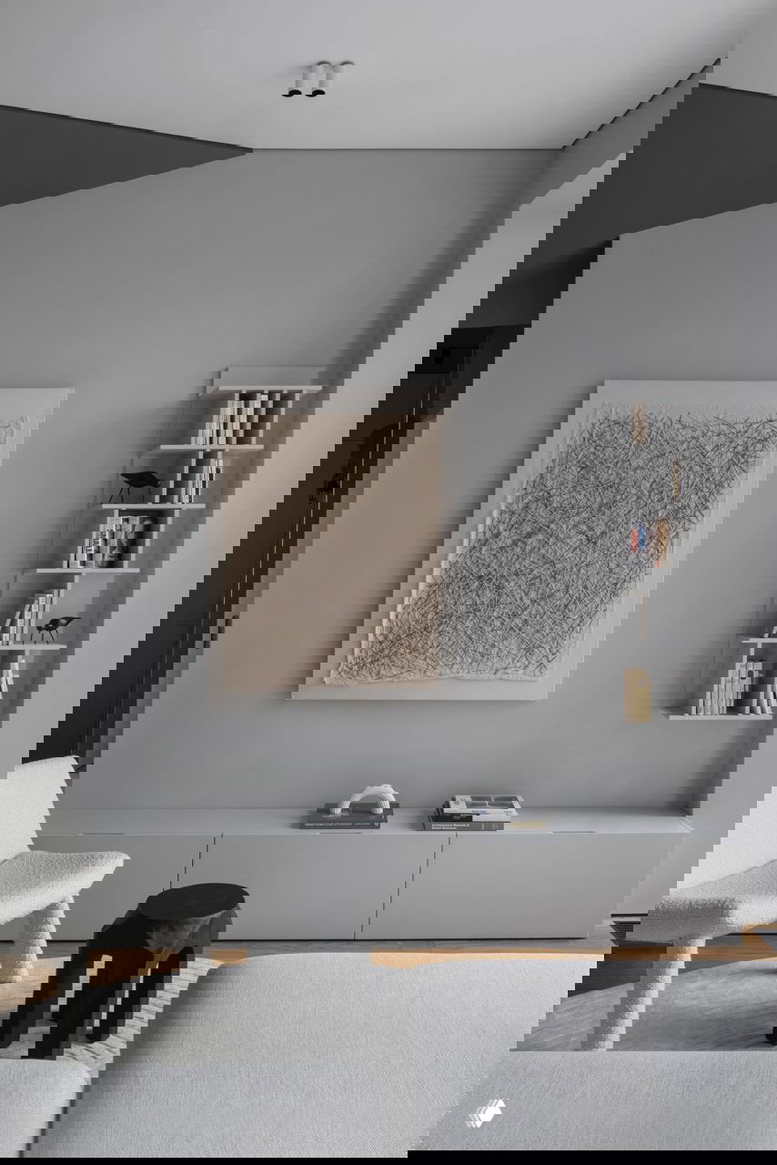 Гостиная зона с серой облицовкой стены, абстрактной картиной и низкой тумбой; деревянный пол и сдержанная мебель создают спокойный фон интерьера.