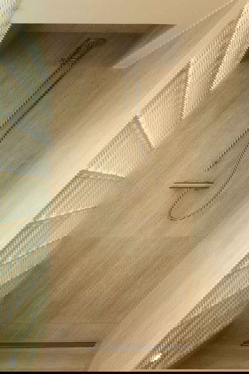 Душевая зона с травертиновыми стенами и стеклоблоками: бежевая плитка, скрытое освещение и современный душевой гарнитур в минималистичной отделке.