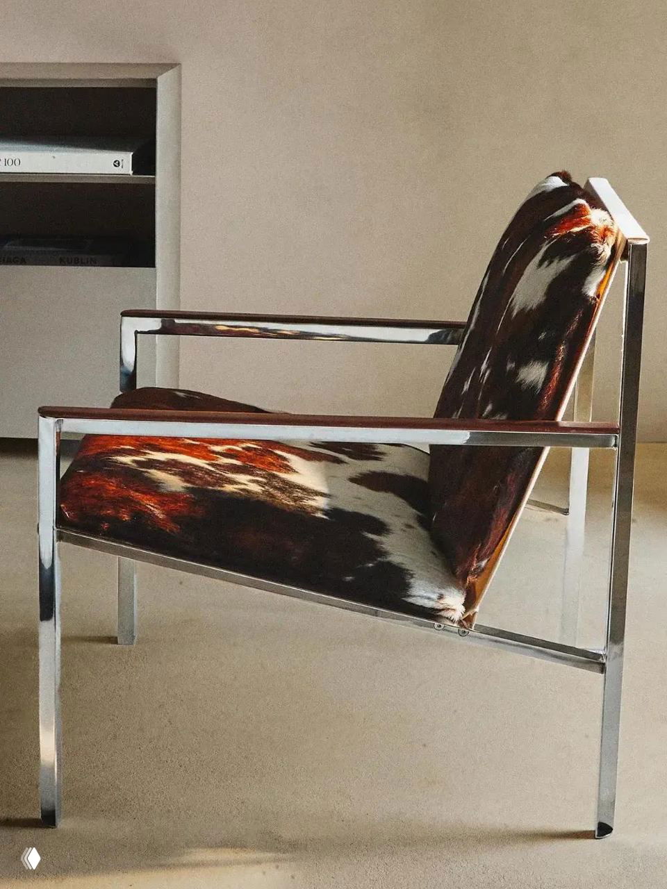 Кресло с хромированной рамой и обивкой из шкуры коровы, расположенное в светлом помещении — сочетание металла и натуральной текстуры в меблировке.