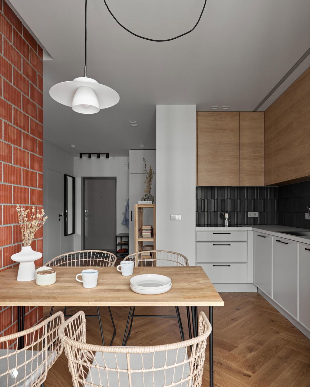 Обеденная зона и кухня с акцентной красной кирпичной стеной, деревянным столом и ротанговыми стульями — открытая планировка и натуральные текстуры.