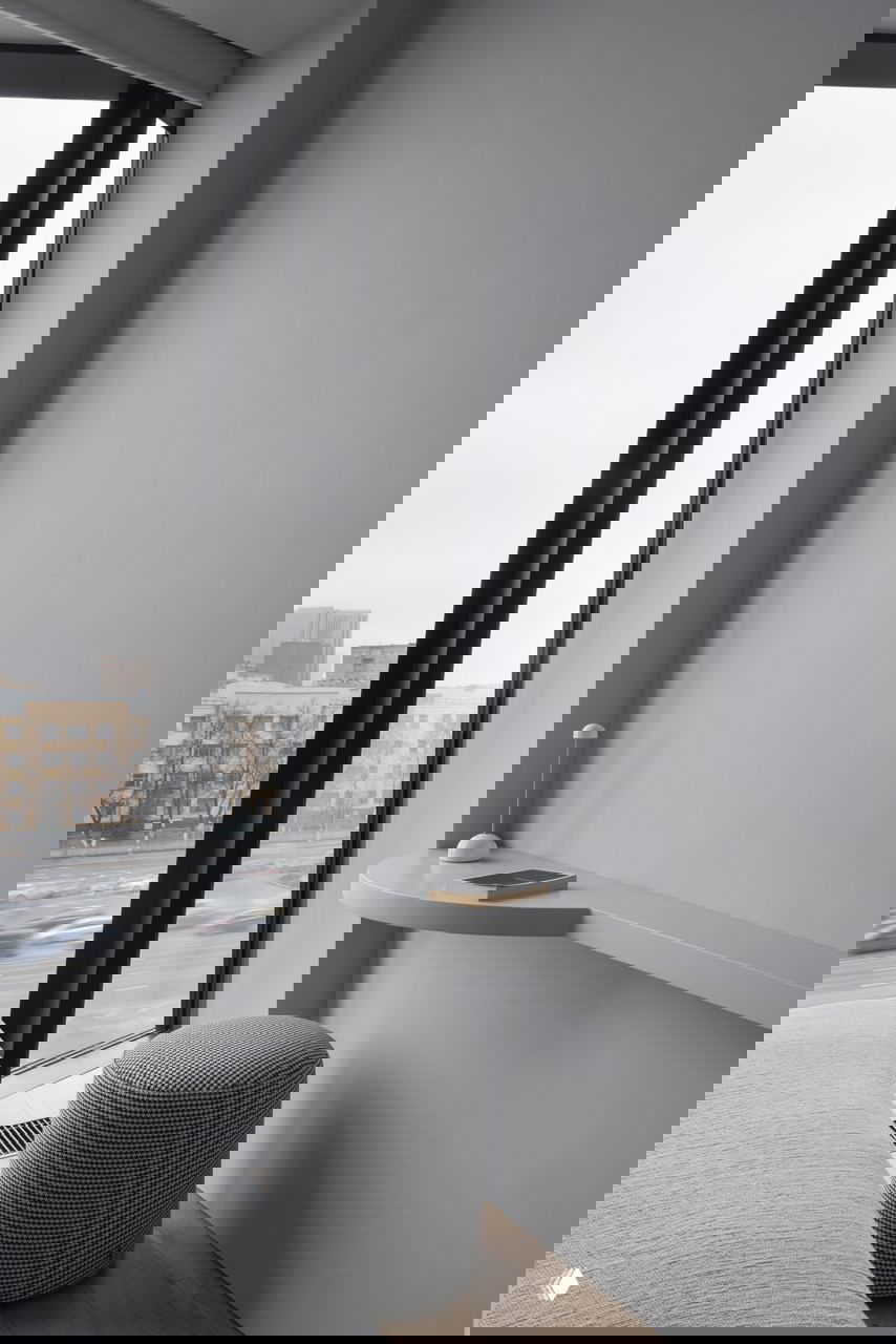 Угловая рабочая зона у окна с полукруглой столешницей и мягким пуфом: компактный функциональный уголок с видом на улицу в общем сером решении квартиры.