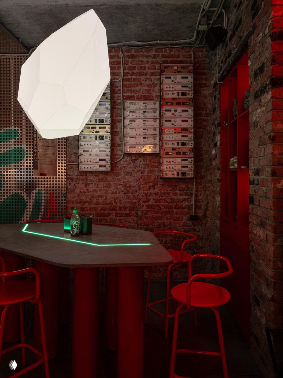 Интерьерный уголок с крупной подвесной лампой, кирпичной стеной и декоративными панелями, красные стулья и неоновая линия на столе.