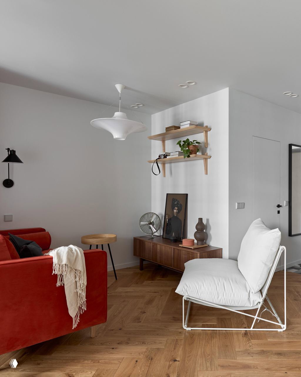 Гостиная зона с ярким красным диваном, белым креслом, низкой деревянной тумбой и аксессуарами в современно-ностальгическом стиле на паркетном полу.