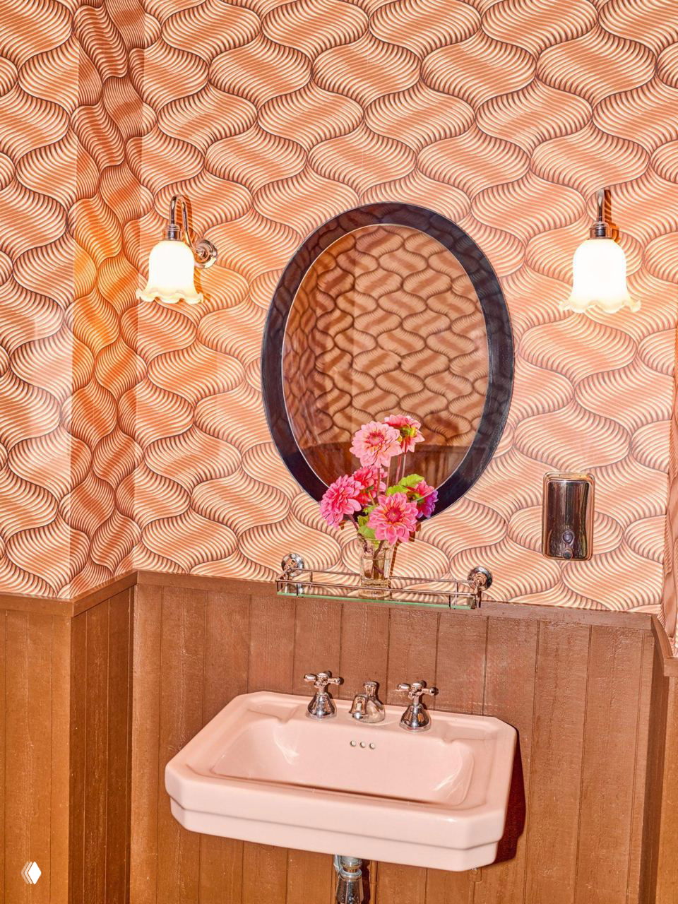 Розовая раковина в туалете ресторана на фоне обоев с волнообразным узором и декоративной зеркальной нишей.