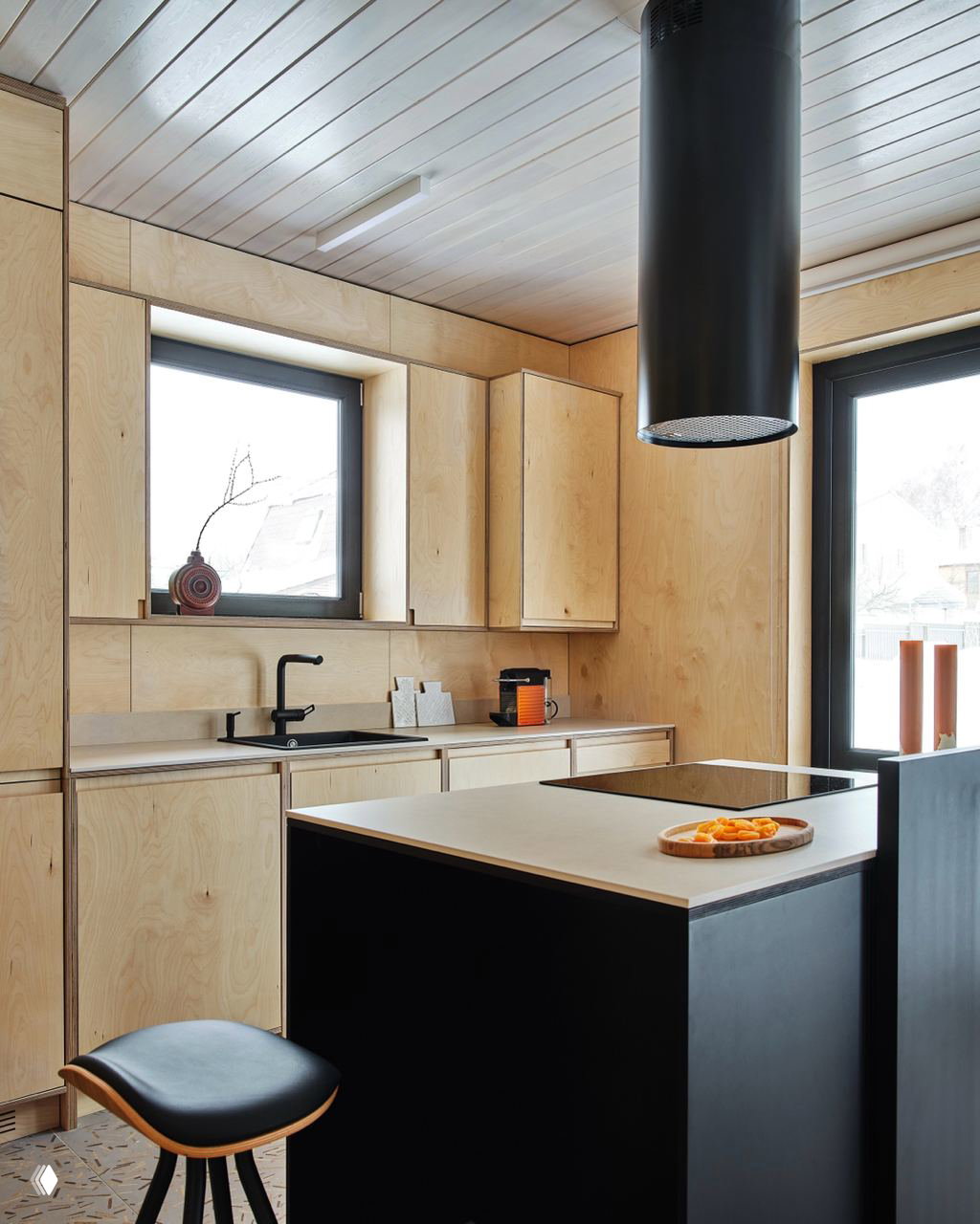 Угловая кухня с матовой варочной панелью и островом с тёмной столешницей; фасады и стеновые панели выполнены из фанеры, вытяжка подчёркивает современную планировку.
