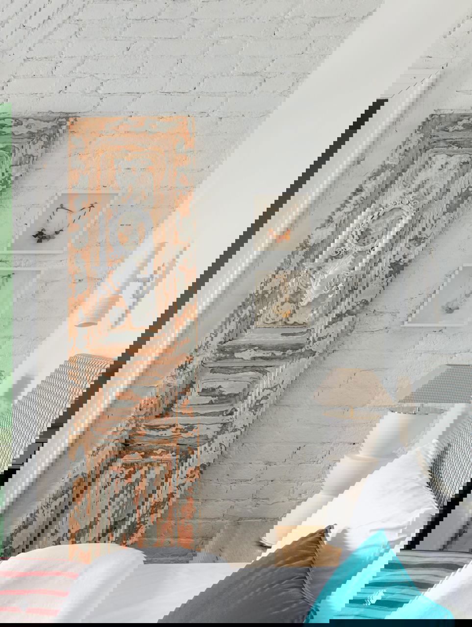 Спальня с белой кирпичной стеной, восстановленной декорированной дверной створкой в технике потертости и мягкой пастельной текстурой постельных тканей.