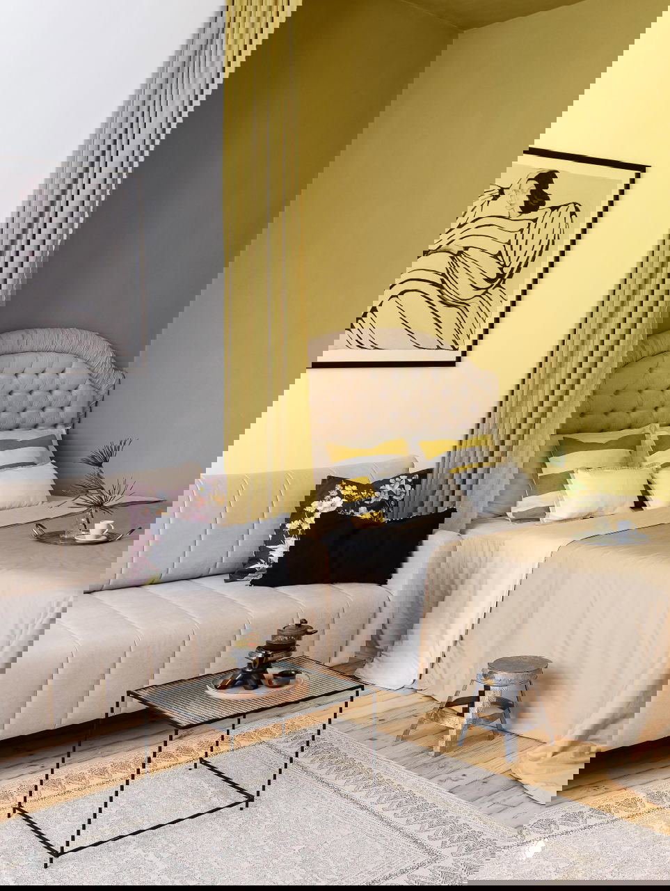 Уютный уголок студии: бежевый диван рядом с кроватью, желто-оливковая акцентная стена и тюль как мягкая перегородка между зонами, тёплые текстуры.