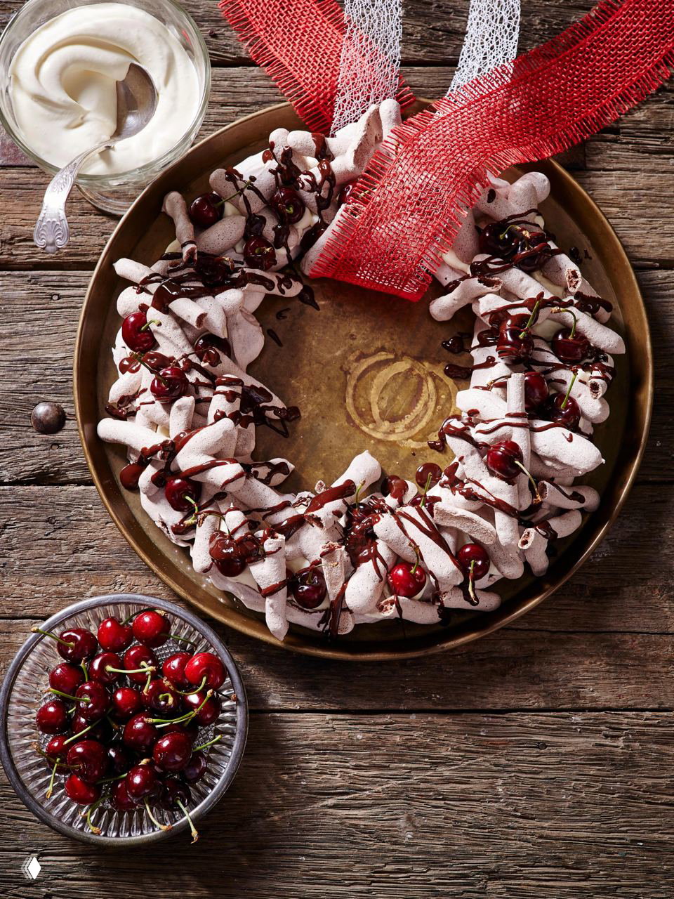 Пышный венок из безе, политый шоколадом и украшенный вишнями; праздничная съедобная композиция на деревянном фоне с текстурой.