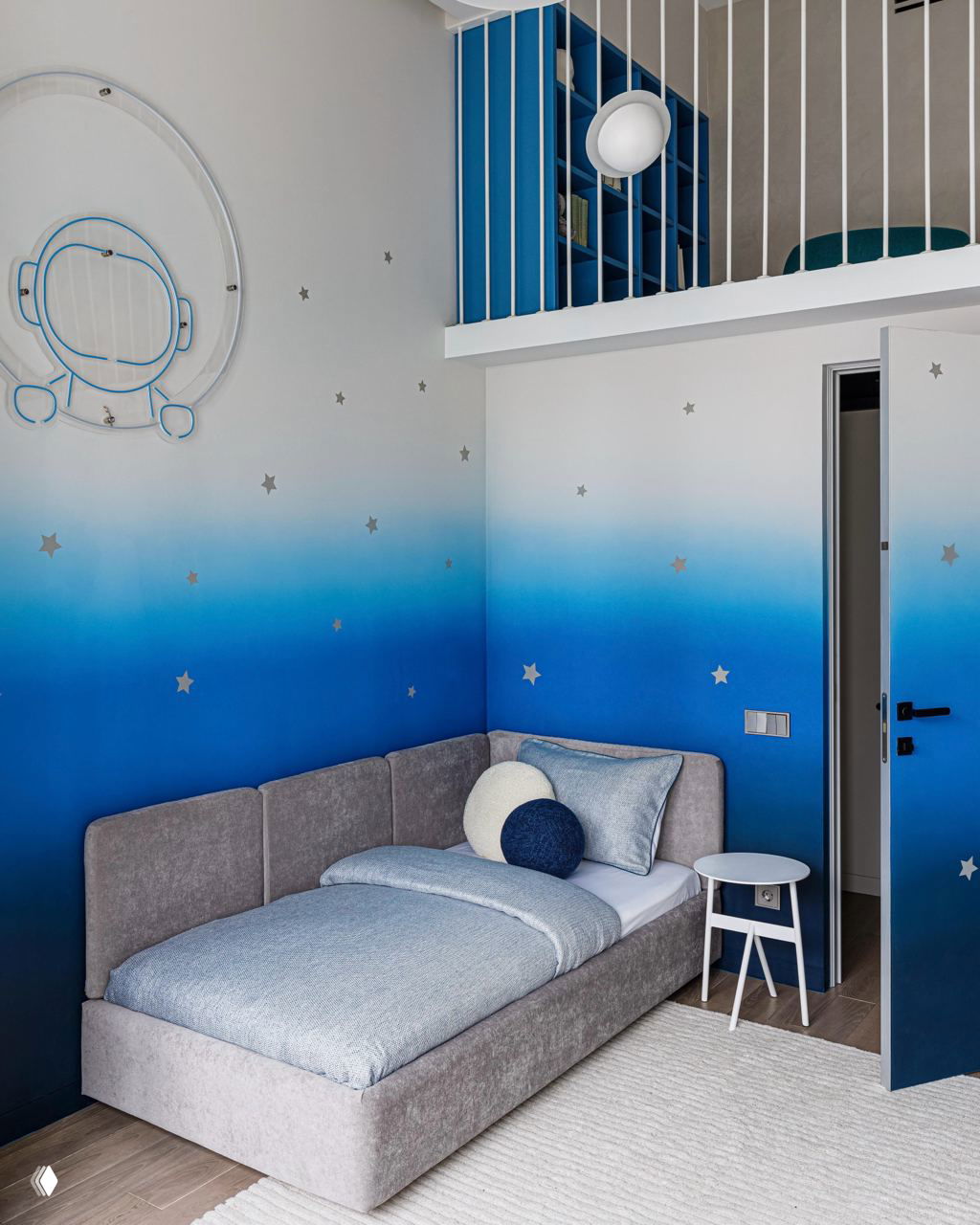 Комната с омбре-градиентом синего на стенах, односпальная кровать и мягкие декоративные подушки в пастельных оттенках — нежная детская тема.