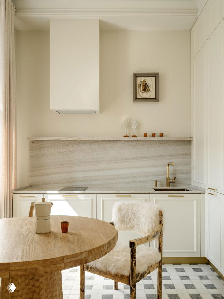 Кухонный уголок: круглый резной стол, стул с меховой отделкой, мраморный фартук и латунная арматура в тёплой светлой гамме в проекте Юлии Шакун.
