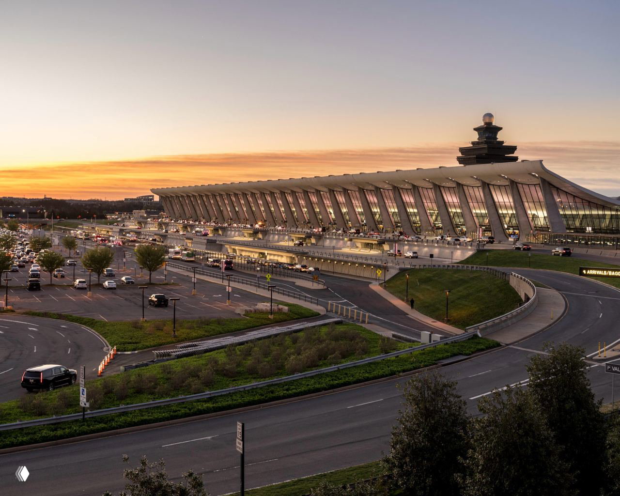 Внешний фасад терминала на закате: длинный корпус с большими стеклянными витражами, подъездная автомагистраль и парковка на переднем плане.