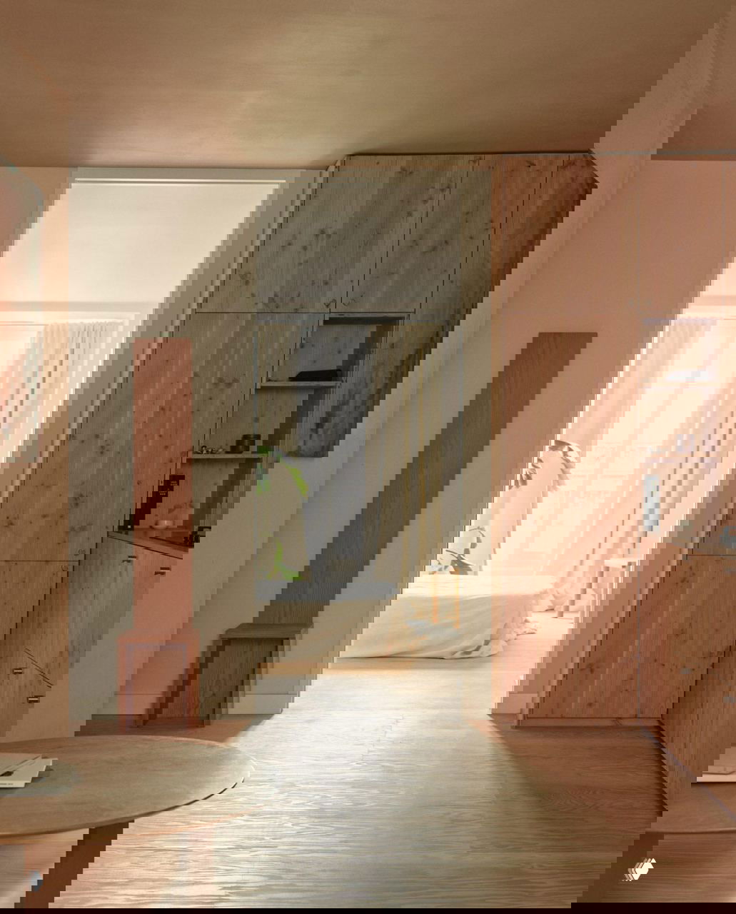 Проход между помещениями: светлая спальня на фоне и встроенные деревянные шкафы с панелями из сосны Дугласа, поднятые дверные коробки до потолка.