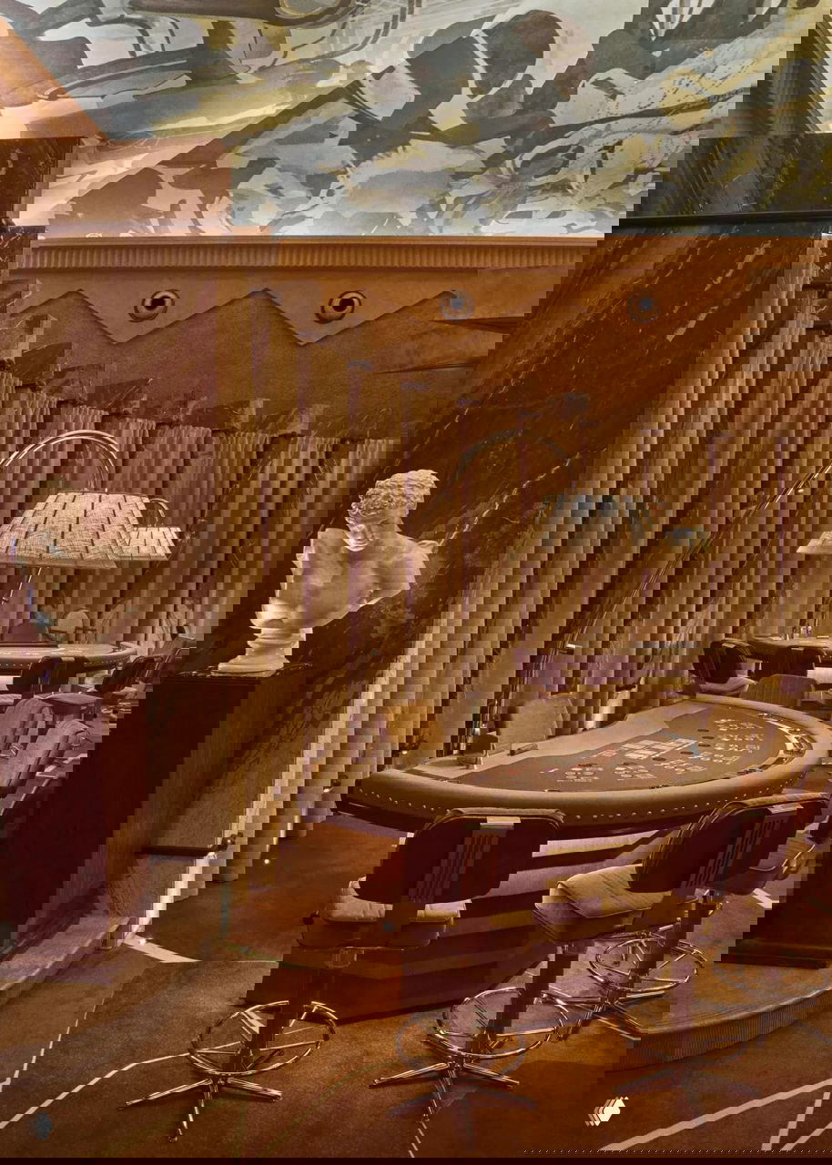 Игровая зона с рулеткой и фишками на фоне фрески на потолке — сочетание театральной сцены и классических игровых столов.