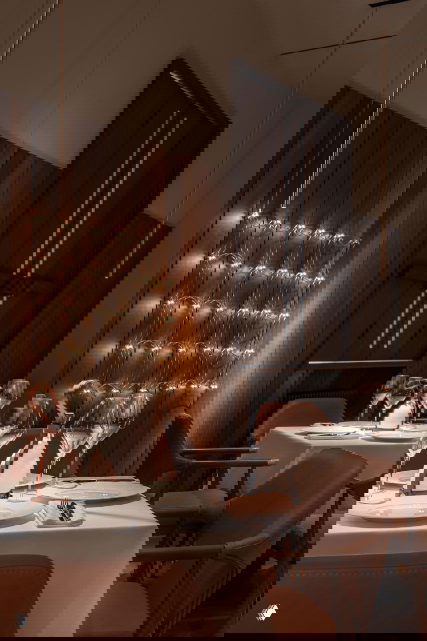 Тёмный уютный зал Savras с тёплой деревянной отделкой, кожаными креслами и сервированными столами в интимной обстановке для вечерних приёмов.