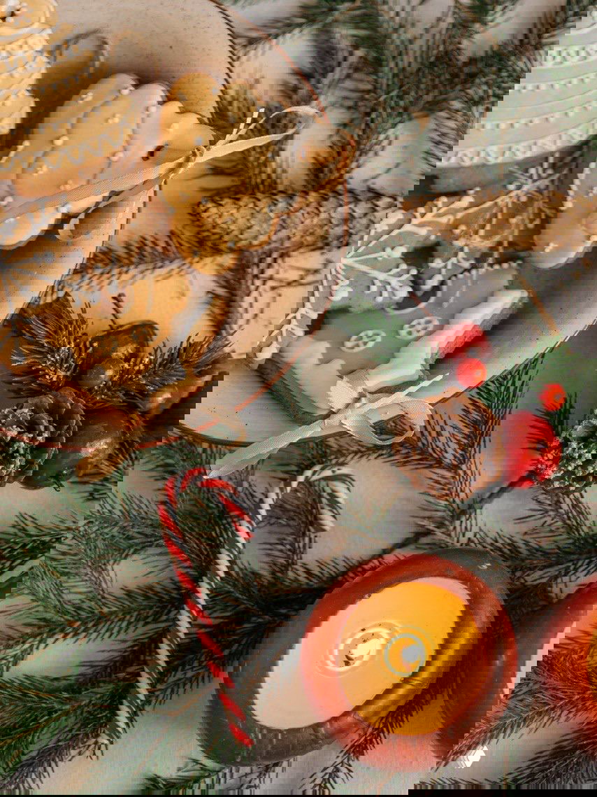 Тарелка с имбирными пряниками, украшенными белой глазурью, рядом зелёные веточки хвои, тросточка и свеча — элементы для праздничной сервировки и ёлочных игрушек.