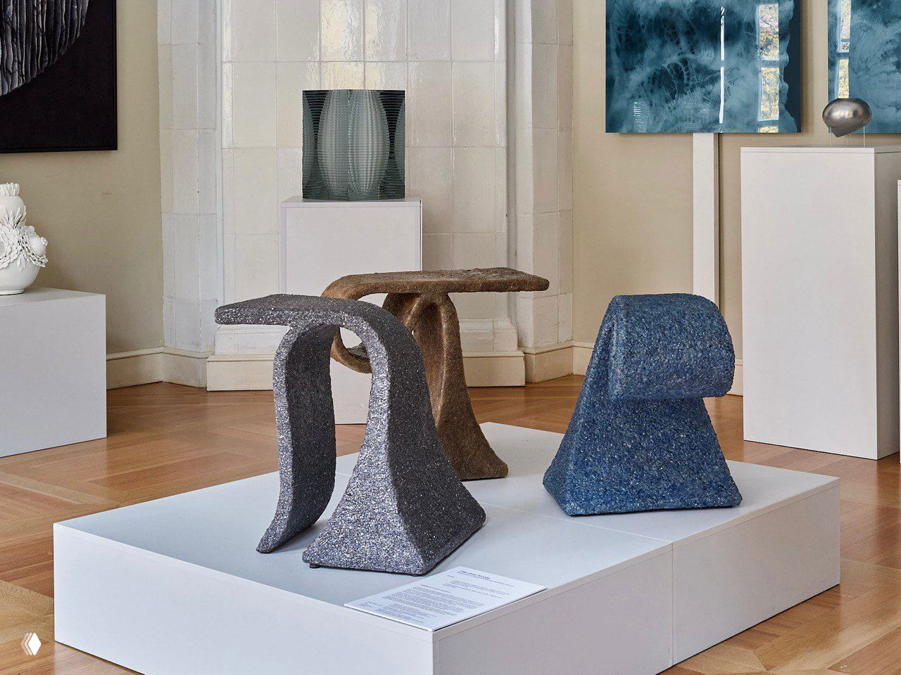Выставочная инсталляция: несколько небольших предметов мебели на белом подиуме в галерее, текстурные покрытия и приглушённая палитра, экспозиция коллекции im-ocean.