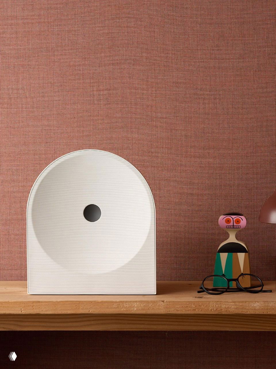 Белая арочная колонка Music Studio 5 стоит на деревянной полке на фоне текстурной обивки, очерчивающей интерьер.