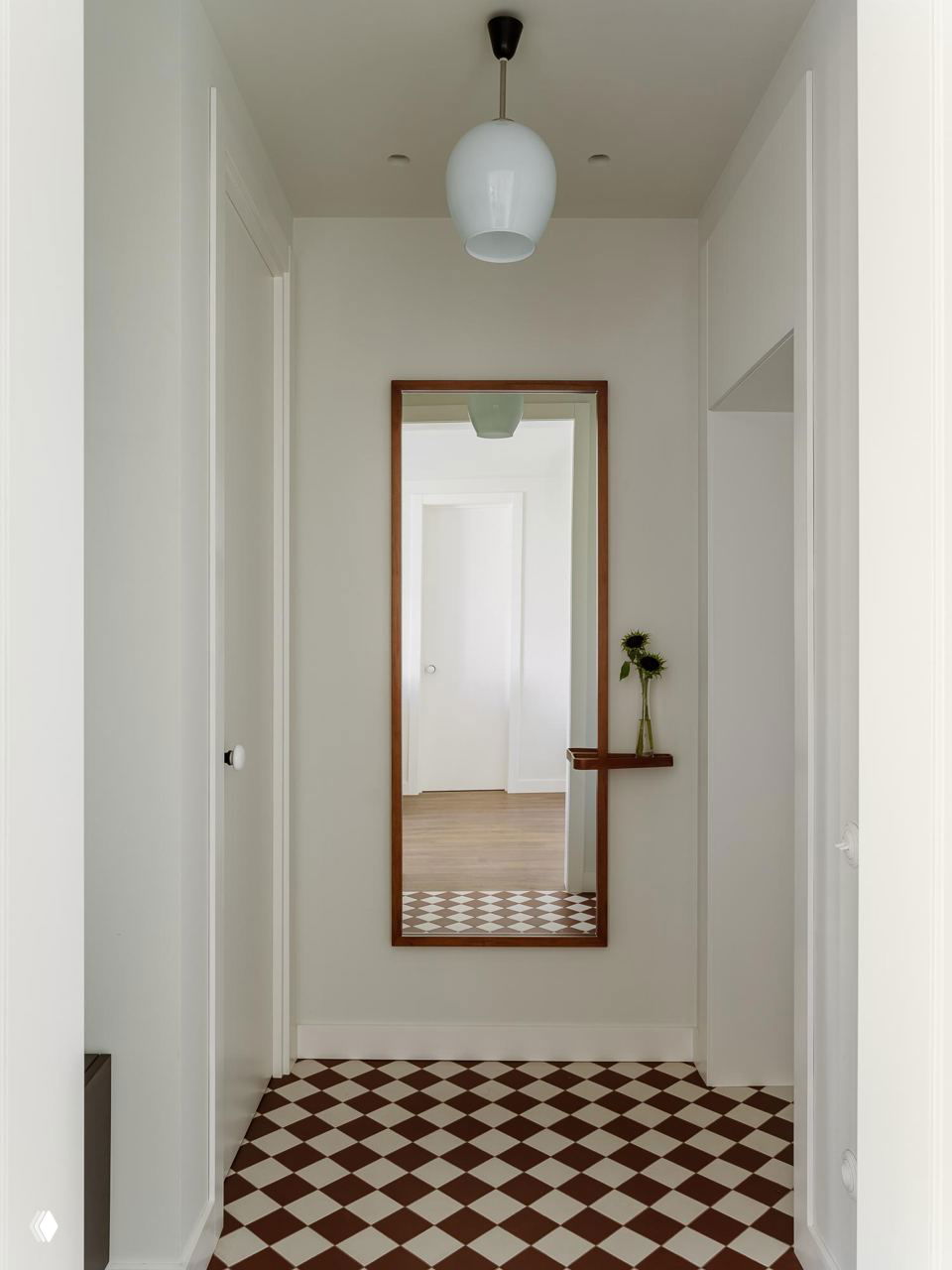 Прихожая с большим прямоугольным зеркалом, небольшой полкой и коричнево-белой шахматной плиткой на полу — акцент на ретро-полы и простые формы.