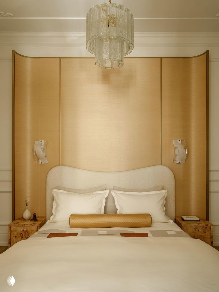 Спальня с высокой мягкой спинкой, золотистой панелью-изголовьем, парными тумбочками из капового дерева и нейтральной текстильной палитрой в проекте Юлии Шакун.