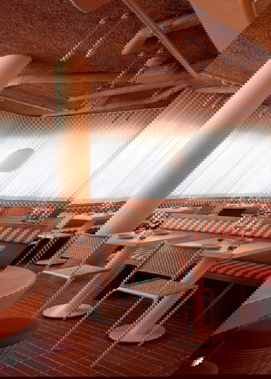 Широкий вид интерьера ресторана с крупными окнами: светлые занавеси, круглые люстры и уютные столики на фоне мягких изгибов стен и колонн