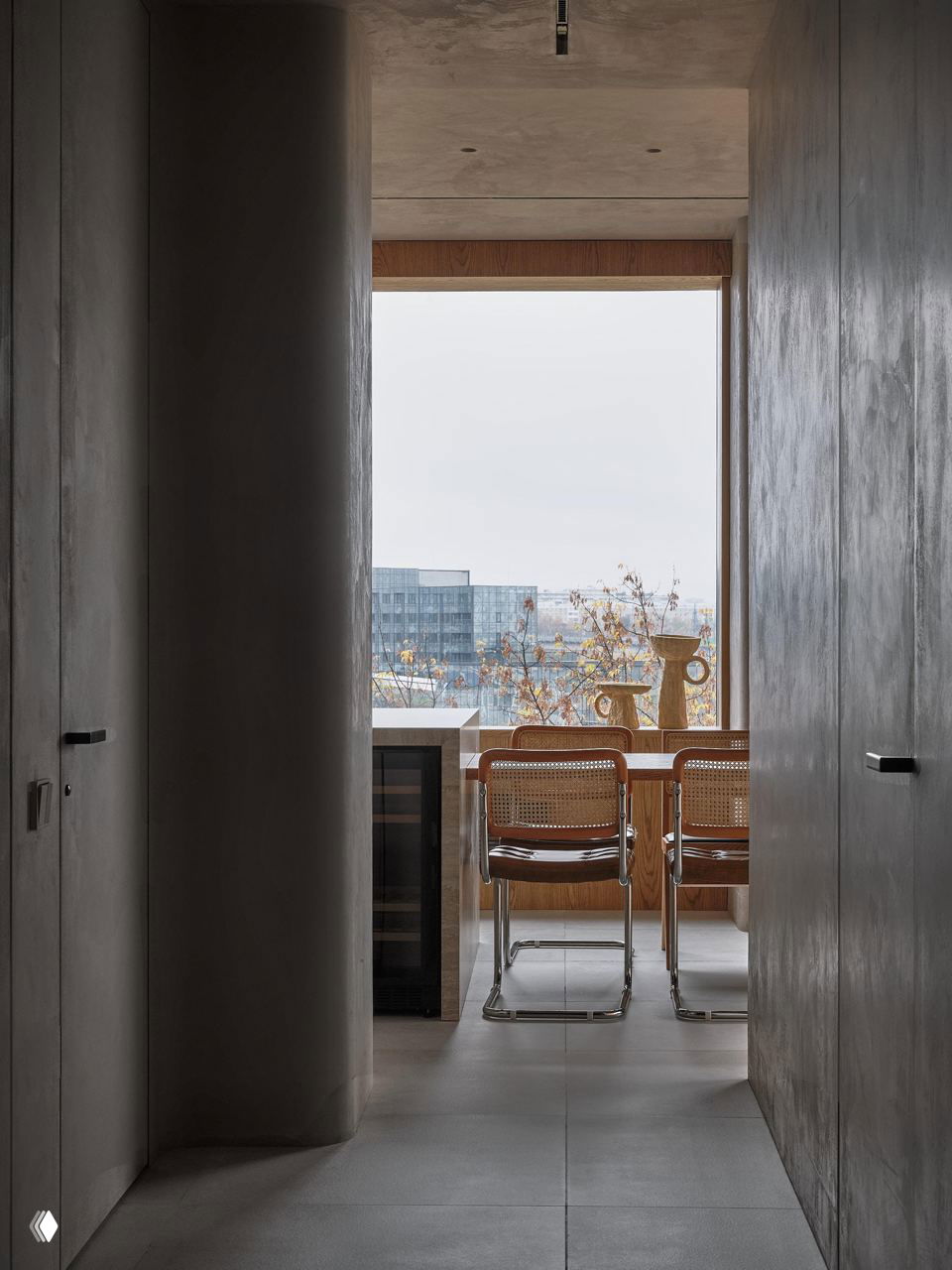 Вид из коридора на кухонно‑столовую зону с большими окнами: хромированные стулья с плетёной спинкой, деревянные элементы и сдержанная цветовая гамма в стиле джапанди.