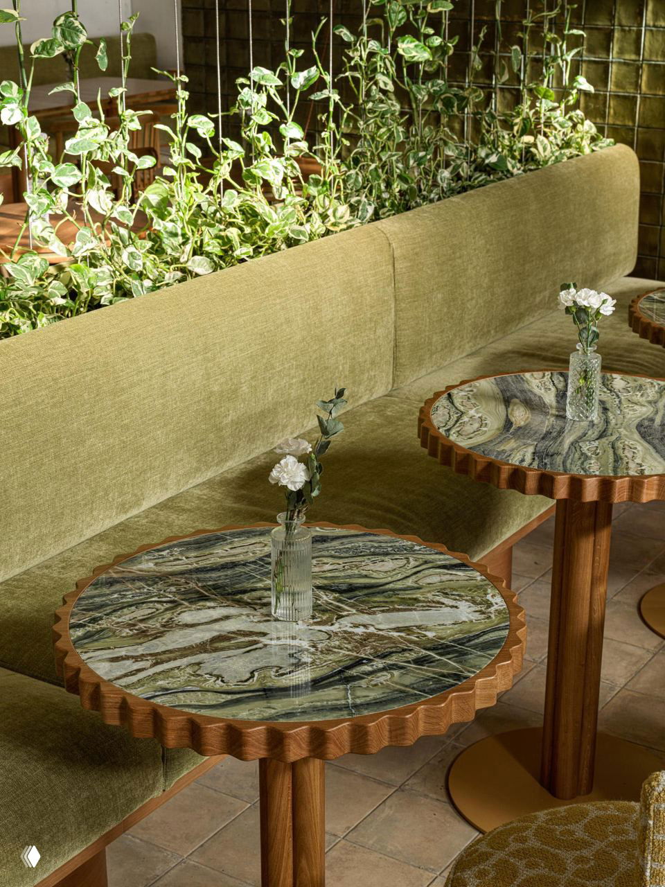 Крупный план дивана и зелёной растительности на перегородке, мраморные столики с резной деревянной окантовкой и небольшие стеклянные вазы с цветами.