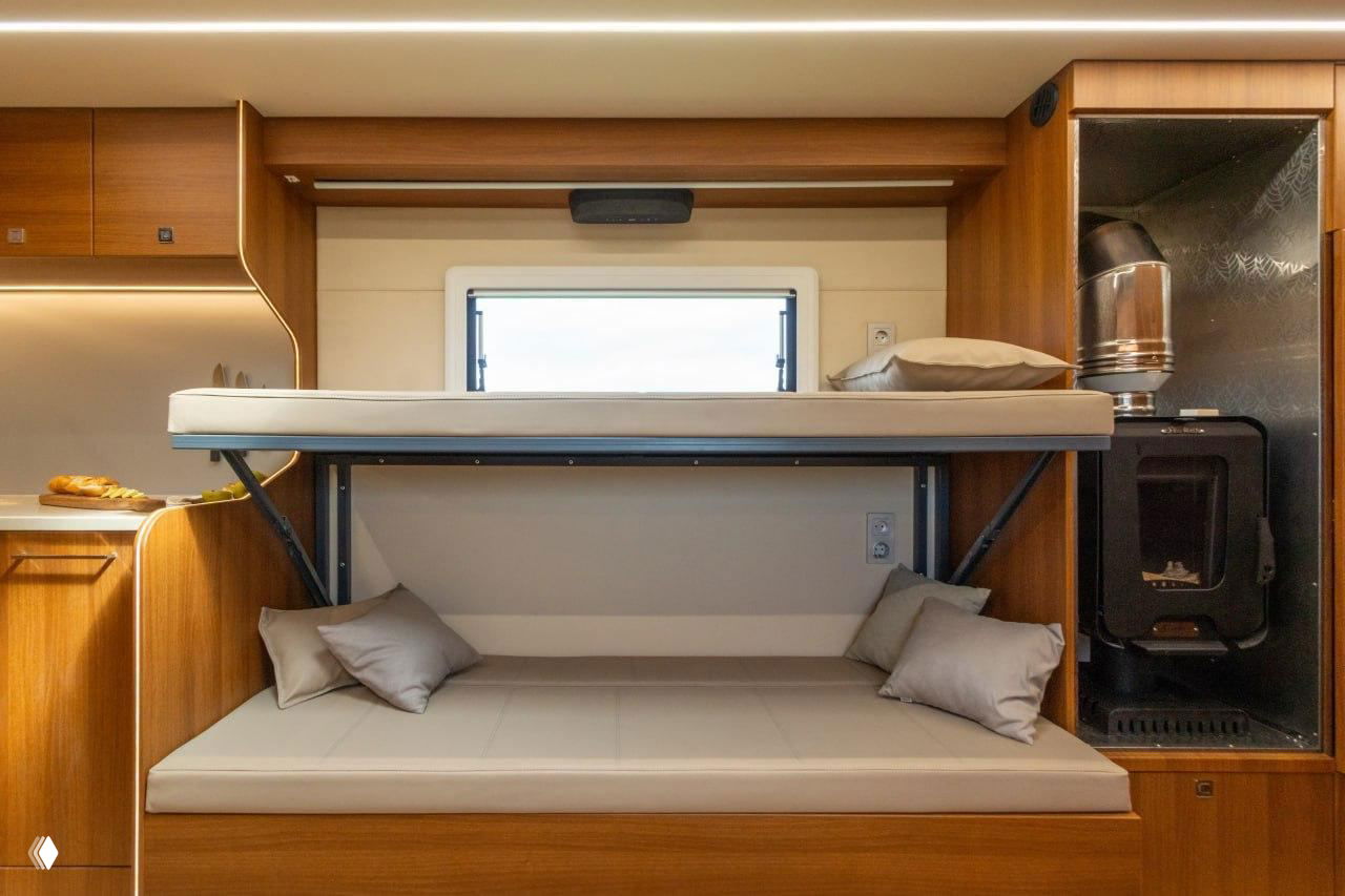 Спальное место с выдвижной верхней кроватью над нижним диваном и печью рядом, компактная организация спальных мест в жилом модуле автодома.