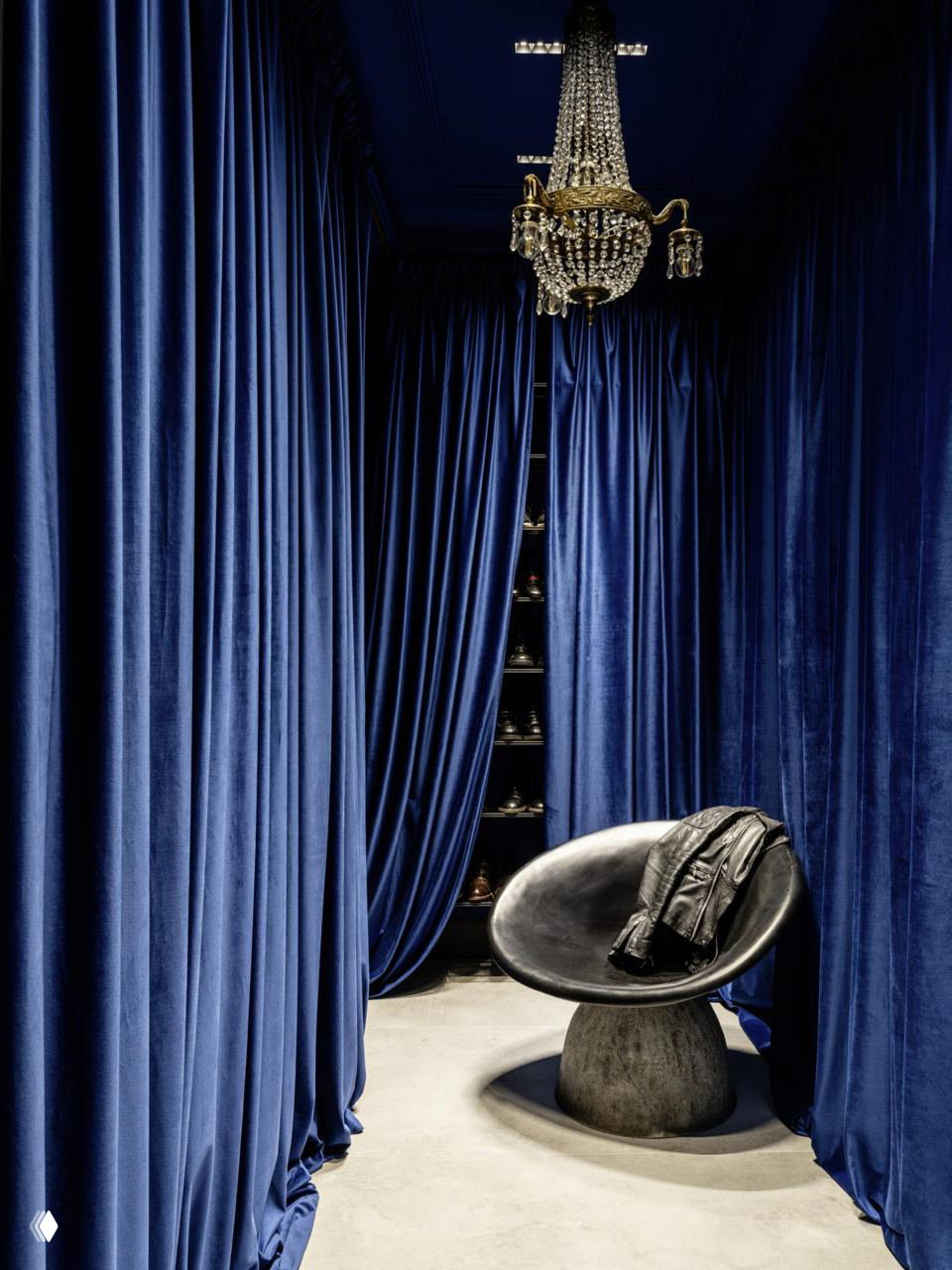 Узкий пример гардеробной-зоны с темно-синими бархатными шторами, хрустальной люстрой и креслом — драматичный интерьерный акцент.