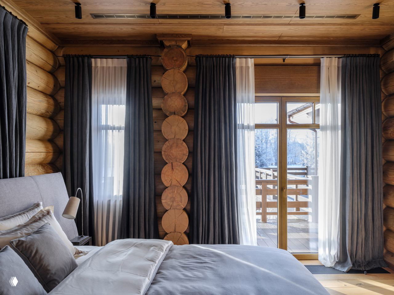 Тёплая древесная отделка в интерьере спальни барачного стиля, круглые бревна на стенах, плотные шторы и выход на балкон с зимним видом