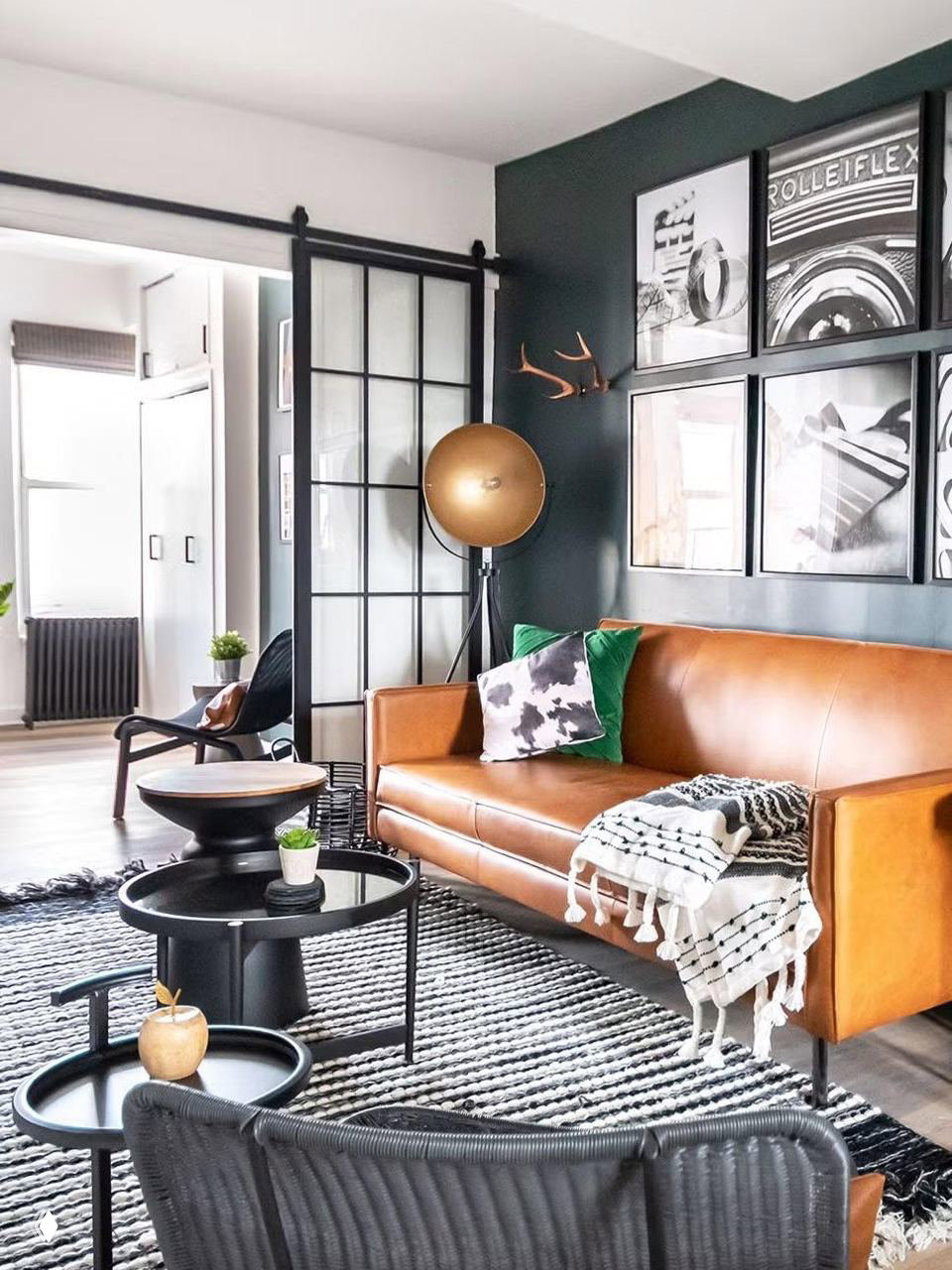 Гостиная-студия с кожаным диваном, тёмной акцентной стеной и стеклянной раздвижной перегородкой в стиле лофта — контрастные текстуры и чёткие границы зон.