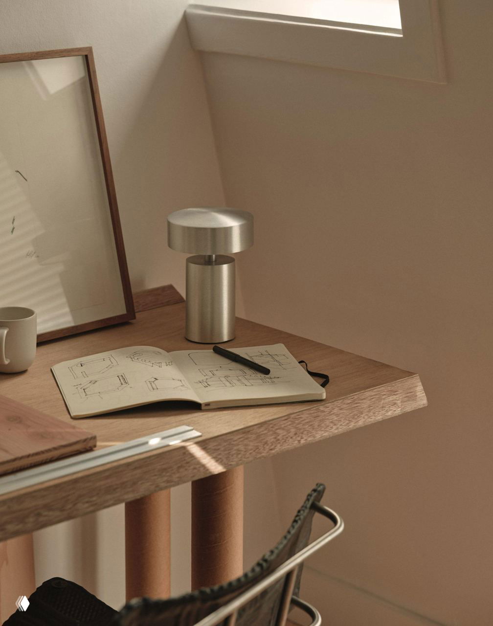 Ближайший план рабочего стола с открытым блокнотом, лампой и инструментами дизайнера; видно текстуру дерева и атмосферное дневное освещение.