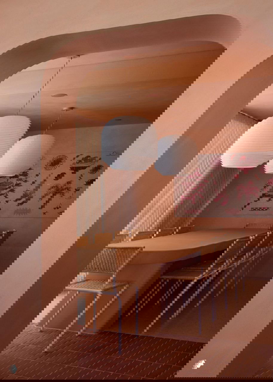 Перегородка и длинный стол в зоне для групповых ужинов: округлые формы, подвесные белые абажуры и терракотовая отделка создают ощущение объятий