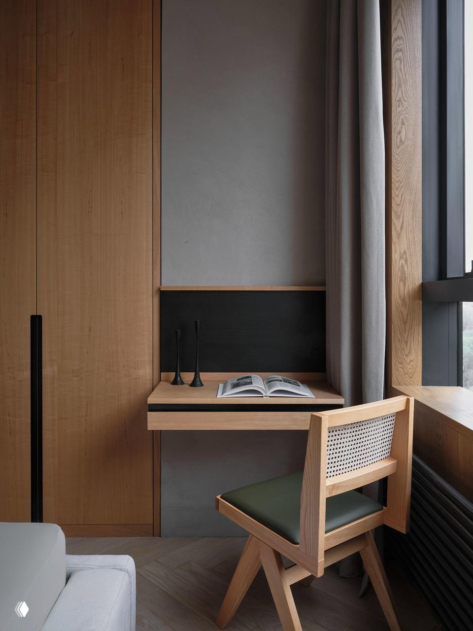 Небольшая рабочая зона у окна: выдвижной настенный стол, шкаф из светлого дерева, стул с плетёной спинкой и книга на рабочей поверхности в сдержанном интерьере.