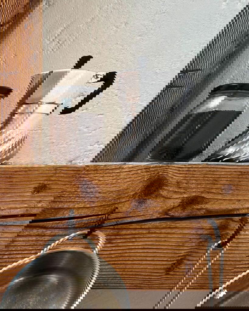 Turbo Moka стоит на деревянной полке рядом с банкой кофе, видна компактная трёхчашечная версия и контраст текстур дерева и металла.