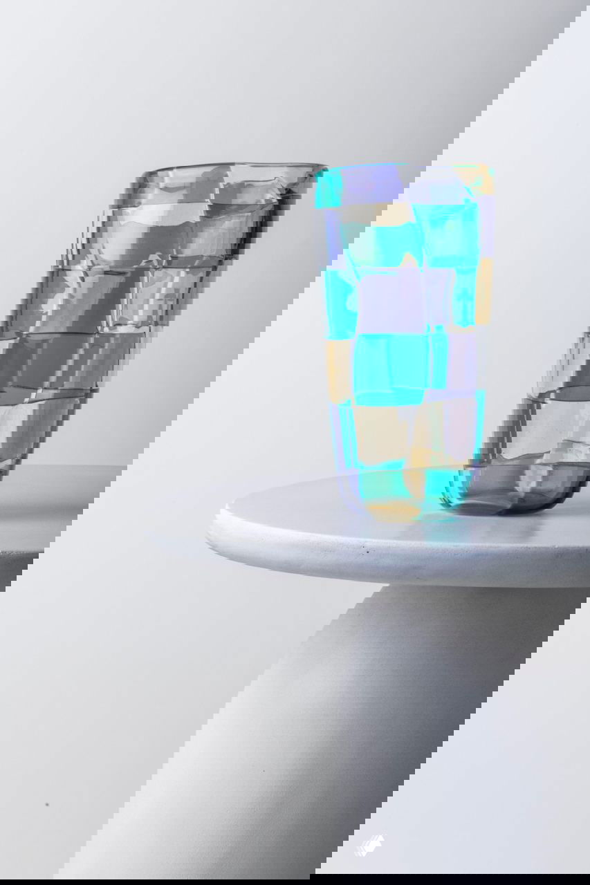 Одиночная высокая ваза из переиздания Pezzati с крупными цветными фрагментами в сиренево-зелено-жёлтой гамме на минималистичном столе.