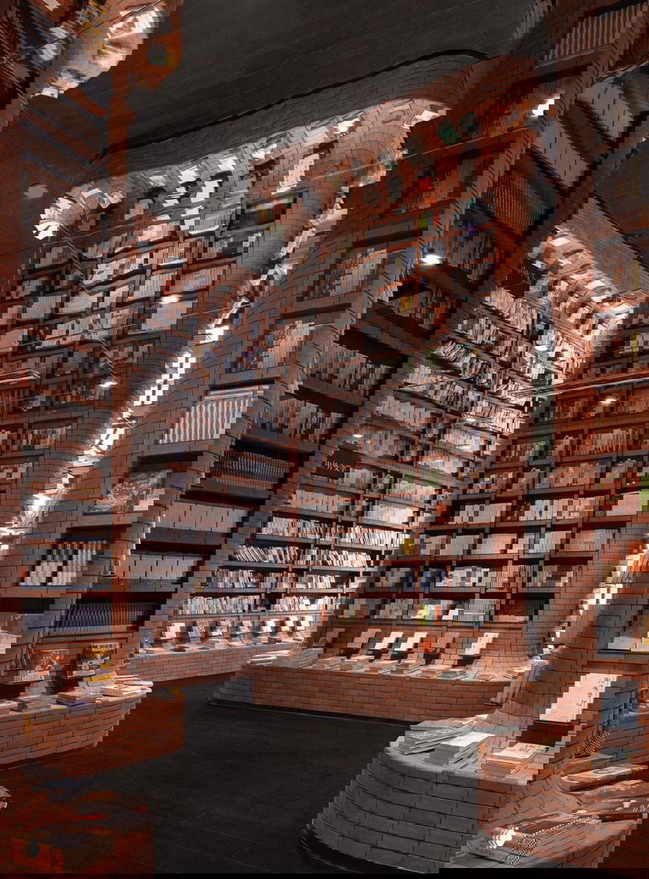 Зона с криволинейными книжными полками и прилавками, облицованными кирпичом; тысячи книг размещены в органичных формах на фоне колонн и арок.