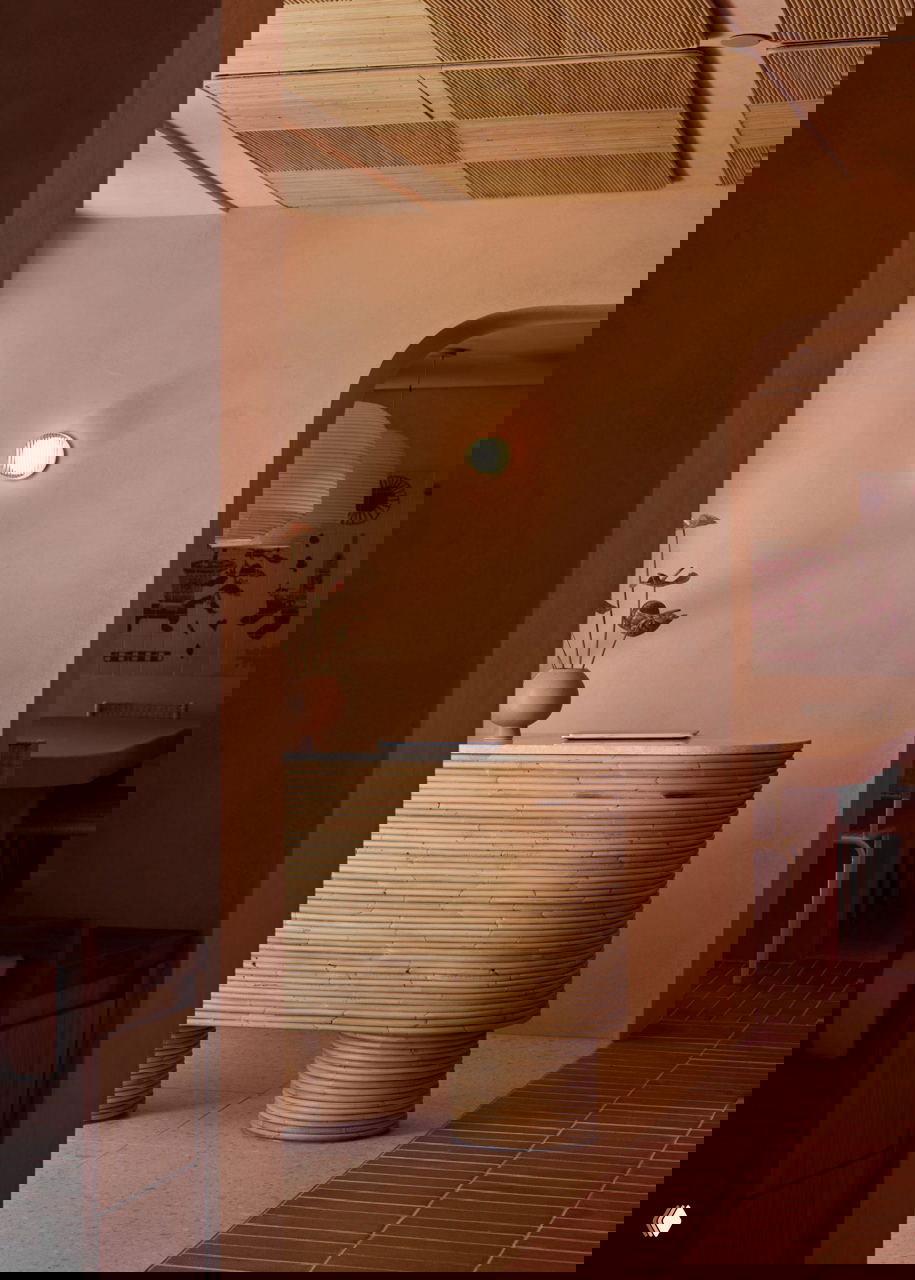 Фрагмент интерьера у входа: мебель из ротанга, округлая стойка ресепшн и спокойная терракотовая палитра с мягкой подсветкой на стенах