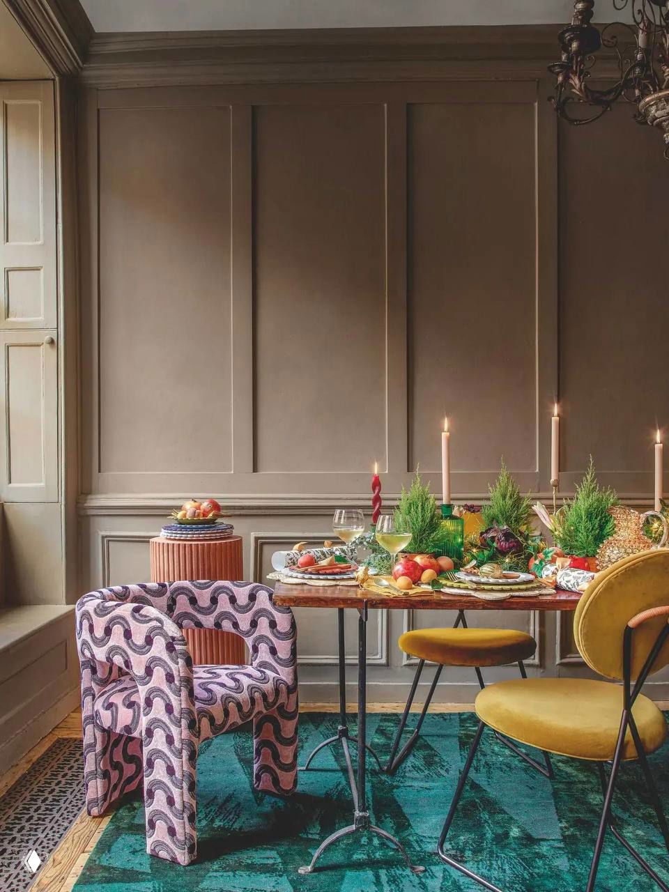 Обеденная зона с цветными стульями и оригинальным ковром: стол украшен свечами, зелёными композициями и сочными фруктами для праздничной сервировки.