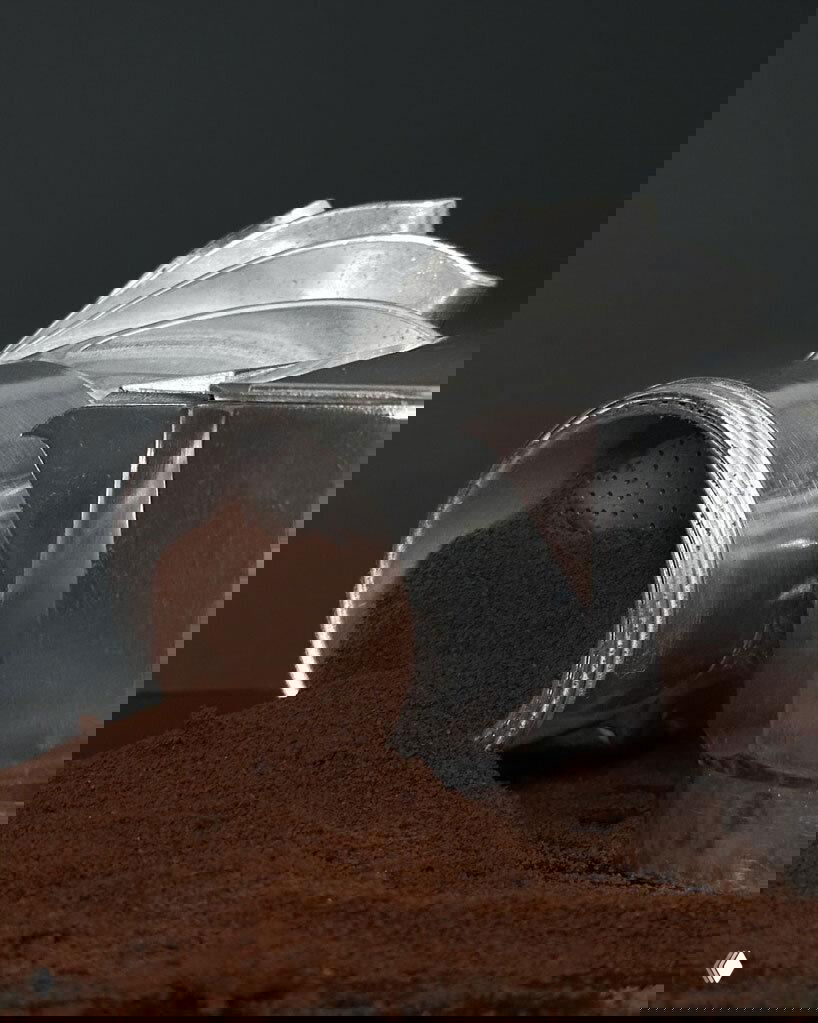 Крупный план разбитой на части кофеварки Turbo Moka с высыпанным молотым кофе, видна внутренняя фильтр-камера и турбинная спиральная часть.