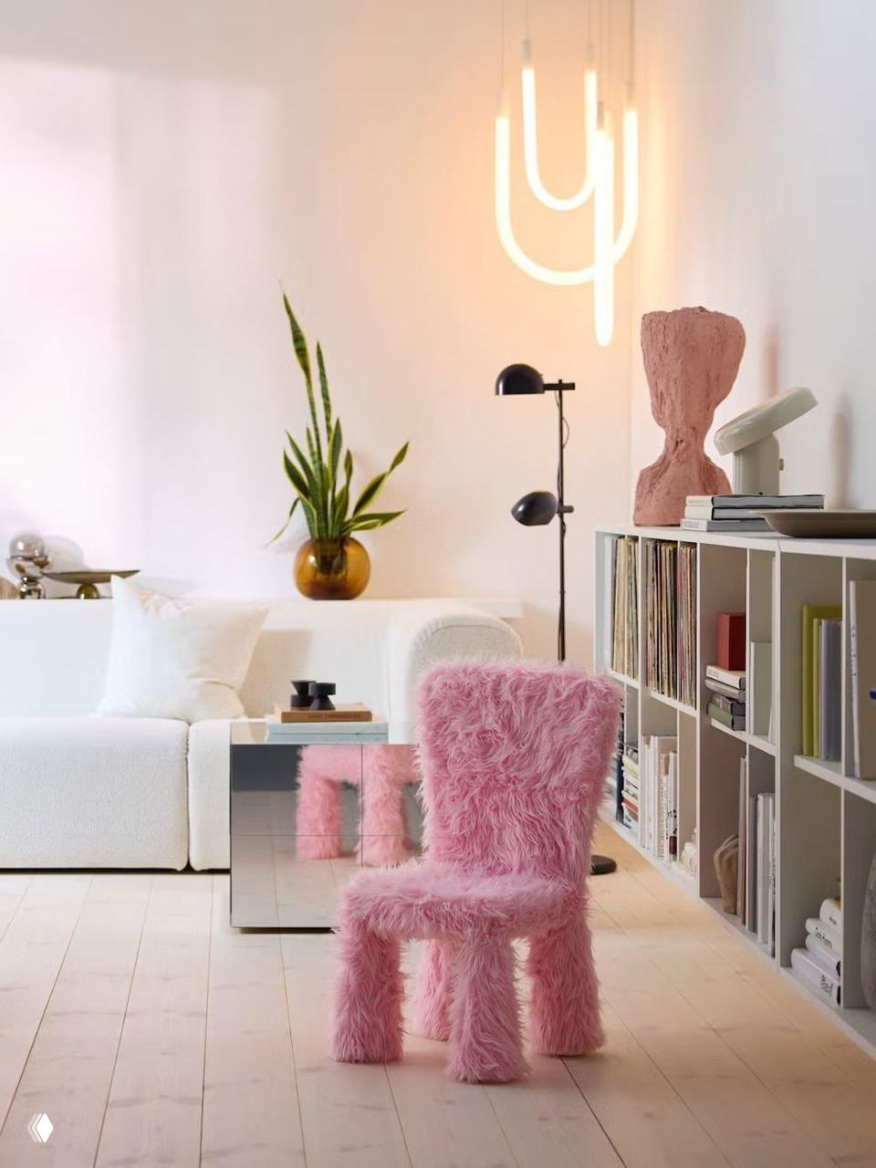 Интерьерная фотография с белым диваном и ярким розовым пушистым детским стулом в оттенке Rebel Pink на светлом деревянном полу и открытыми полками с книгами.