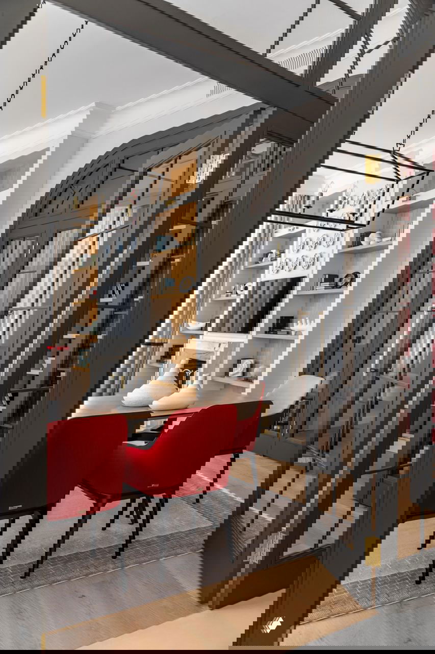 Проход к столовой через чёрные арочные стеклянные двери, ярко-красные обеденные стулья на фоне светлой отделки и деревянного пола в московской квартире.