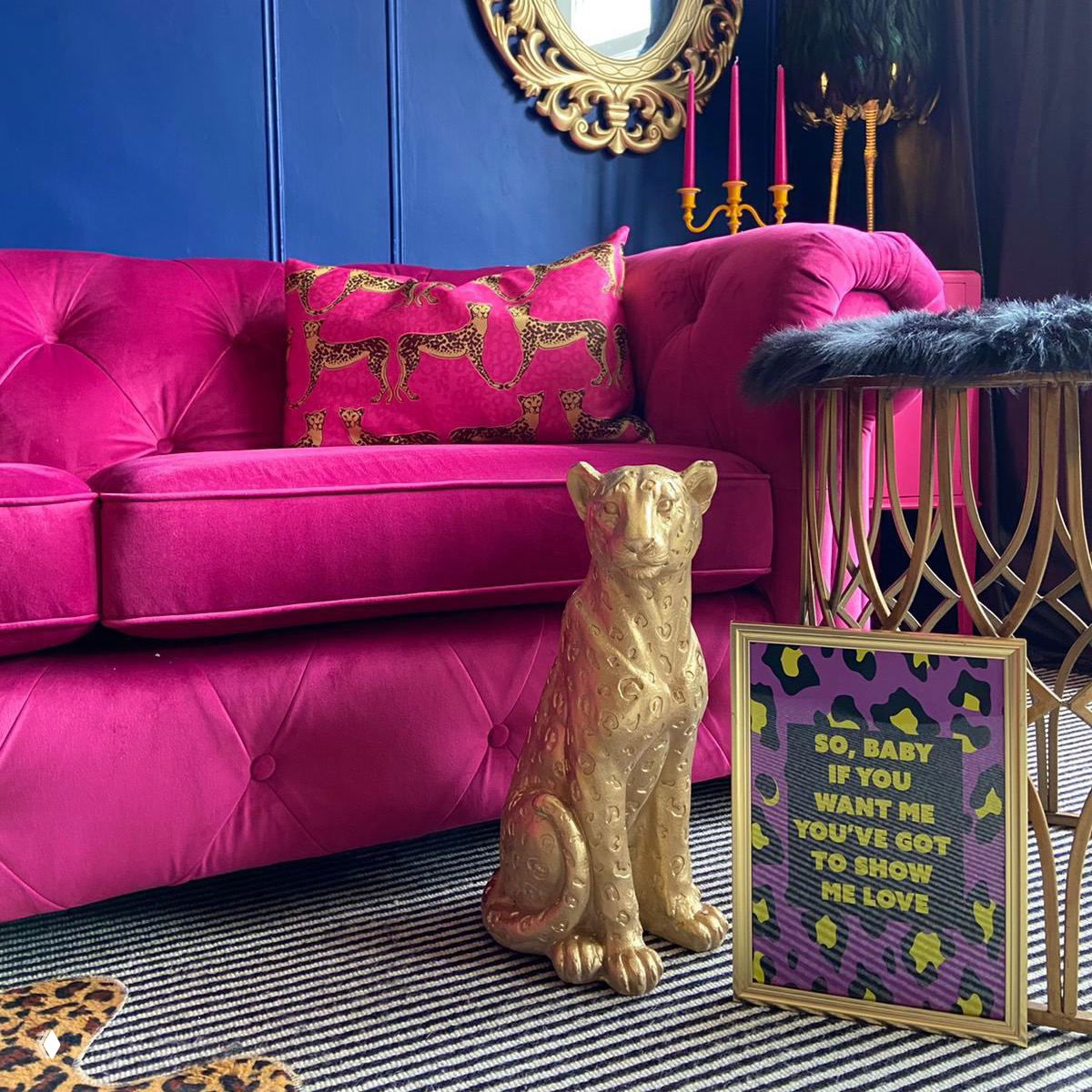 Бархатный фуксия диван на фоне тёмно-синей стены, золотая декоративная фигурка и зеркальная рама — контрастные цвета и богатые текстуры для эффекта драматичности.