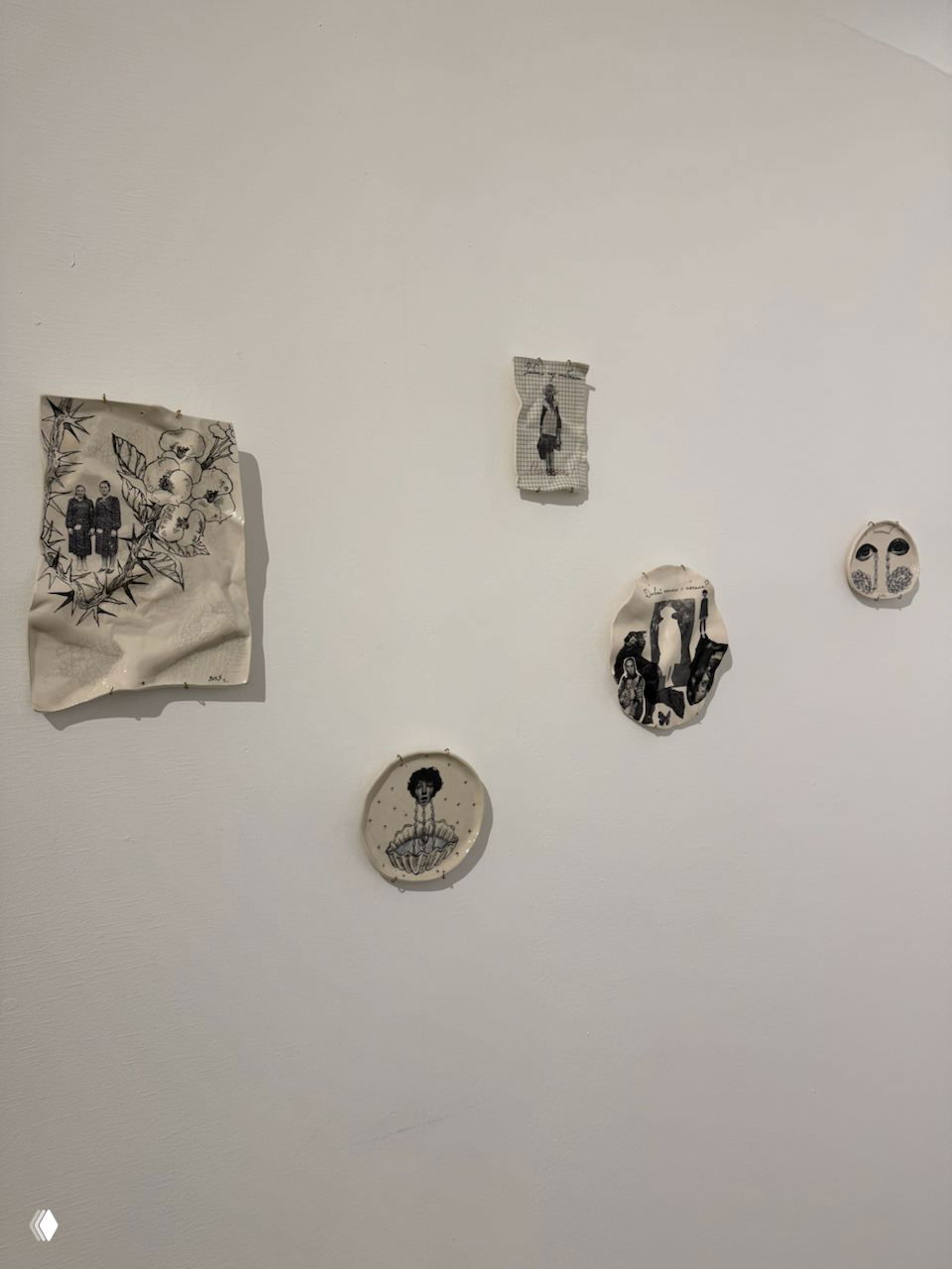 Небольшие чёрно-белые иллюстрации и керамические диски с рисунками, развешенные на белой стене выставочного зала в несколько рядов