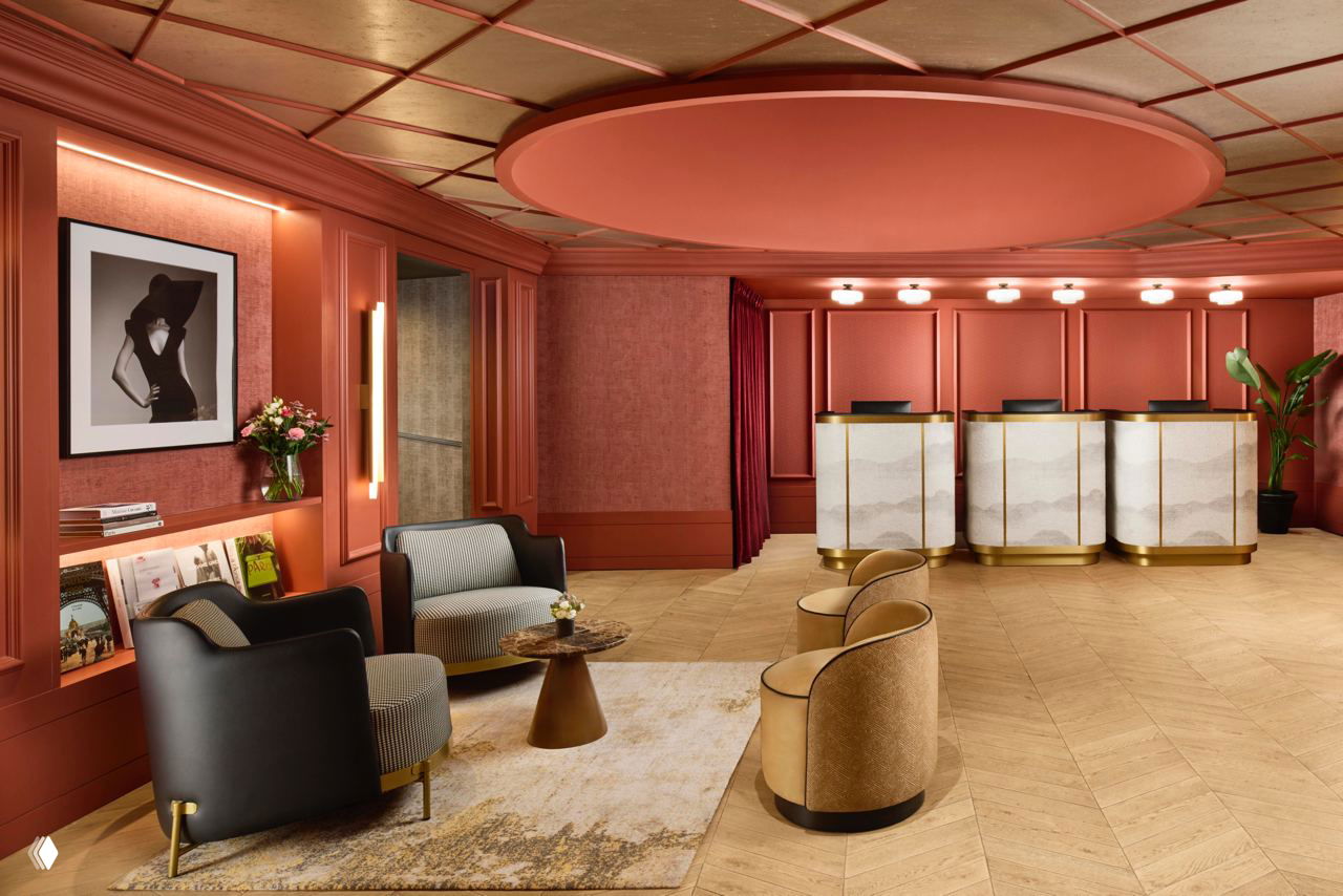 Ресепшн и гостиная зона в тёплой розовой палитре: стойка регистрации, мягкие кресла и крупная черно‑белая фотография на стене.