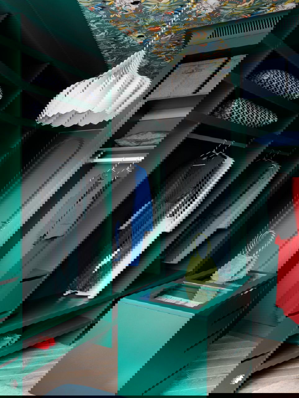 Глубокая изумрудная гардеробная с островком, витиеватыми полками и декоративным потолком — насыщенный цветовой акцент в интерьере хранения.