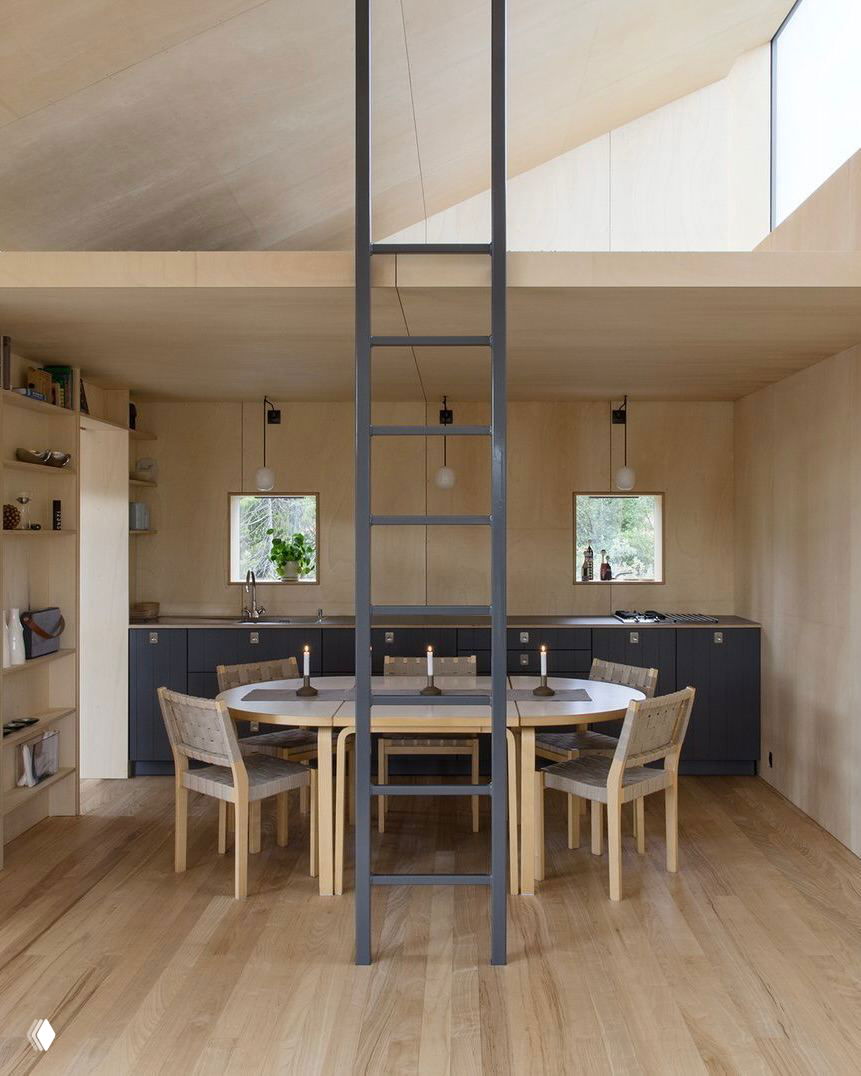 Интерьер столовой хижины Vindheim: светлая фанерная отделка, круглый стол, деревянные стулья и металлическая лестница к антресоли — компактное и продуманное пространство.