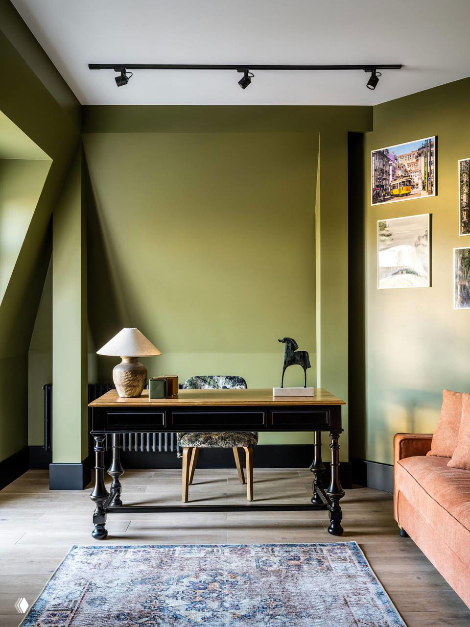 Рабочая зона с антикварным письменным столом на фоне оливковой стены; ковёр у пола, декоративные постеры и тёплый рассеянный свет.