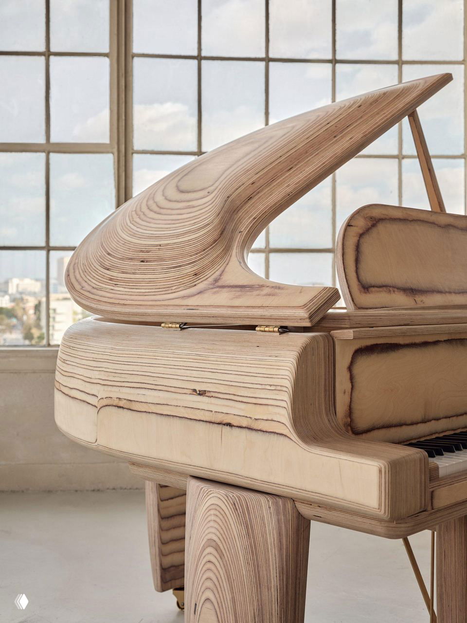 Крупный план крышки рояля Timbra с плавной дюнной формой из ламинированной березы; видно слоистую текстуру древесины.