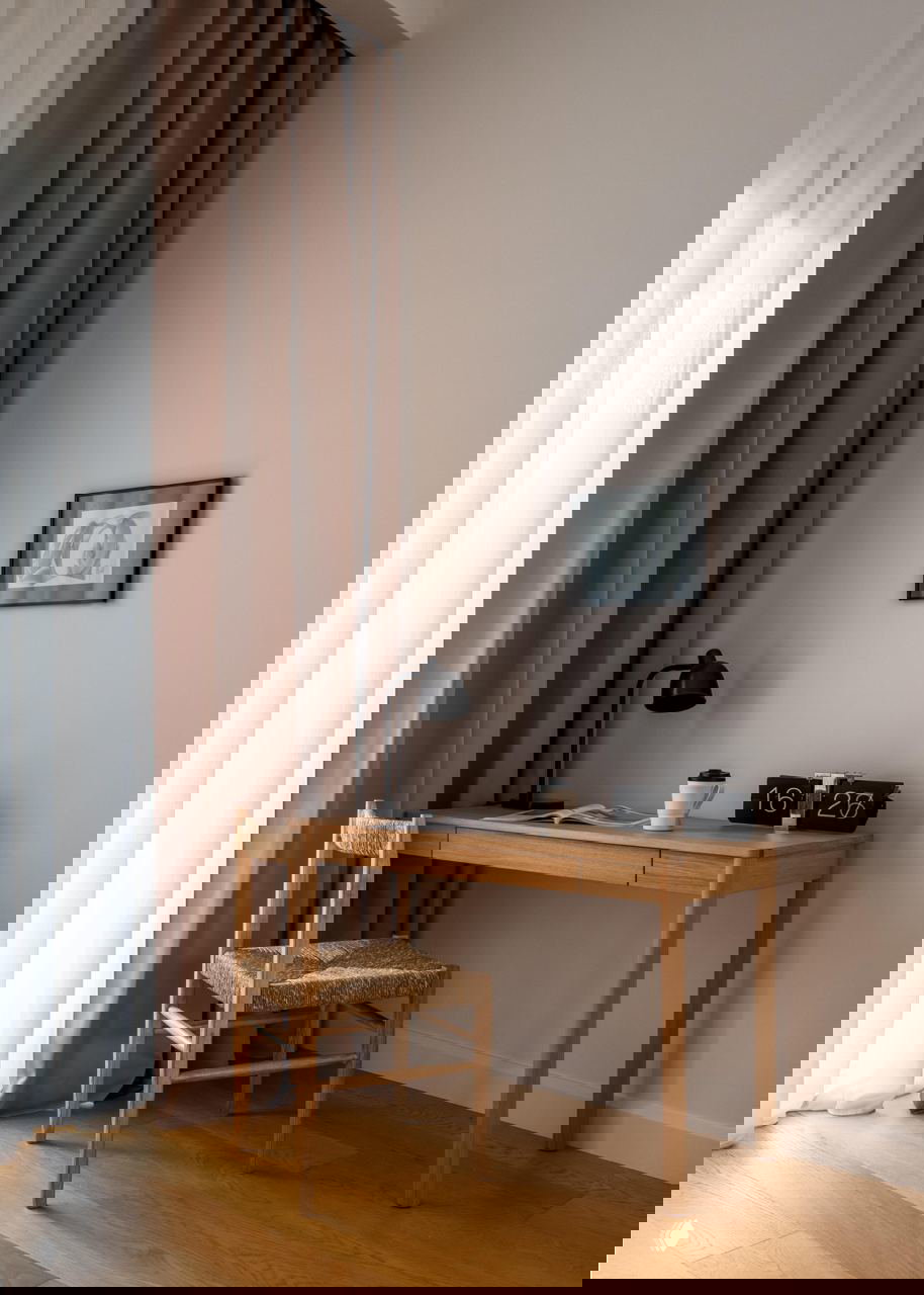 Рабочий уголок в пастельных тонах: деревянный стол, плетёный стул и плотные шторы — минимализм с тёплой терракотовой ноткой.