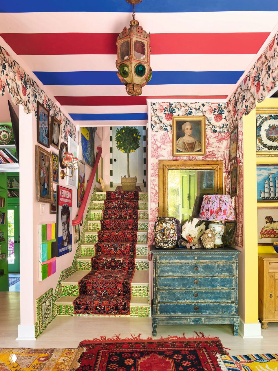 Яркая входная зона и лестница: полосатый потолок, красочная лестничная дорожка, старинный комод и коллаж из картин на стене у ступеней.